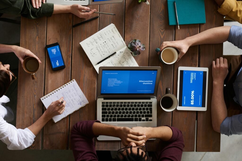 Group of coworkers discussing business strategies with laptops and tablets in a modern office setting.