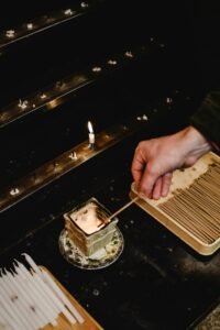 A hand lights incense in a serene Kyoto temple setting, highlighting ritual and spirituality.