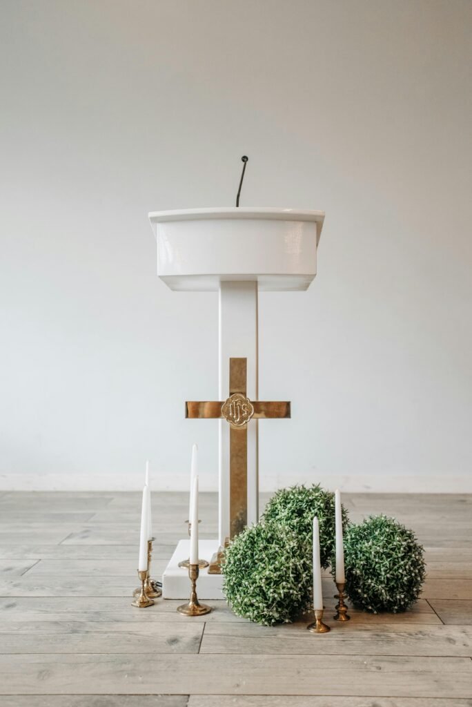 A wooden church altar with gold cross, candles, and plants on a wooden floor. Simple and elegant.