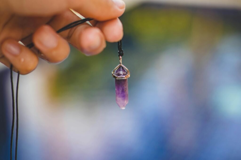 Close-up of a hand holding a purple amethyst pendant against a blurred outdoor background.